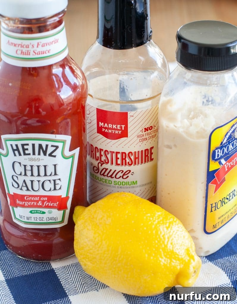 Individual ingredients for homemade cocktail sauce: a bottle of chili sauce, a jar of prepared horseradish, a bottle of Worcestershire sauce, and fresh lemons.