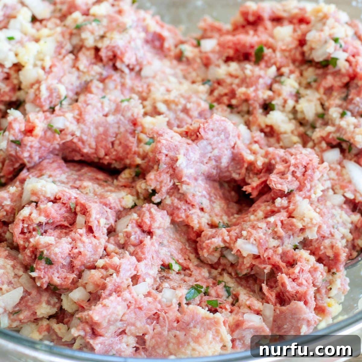 A large silver mixing bowl containing the raw meatloaf mixture, showing the various ingredients uniformly combined and ready for shaping.