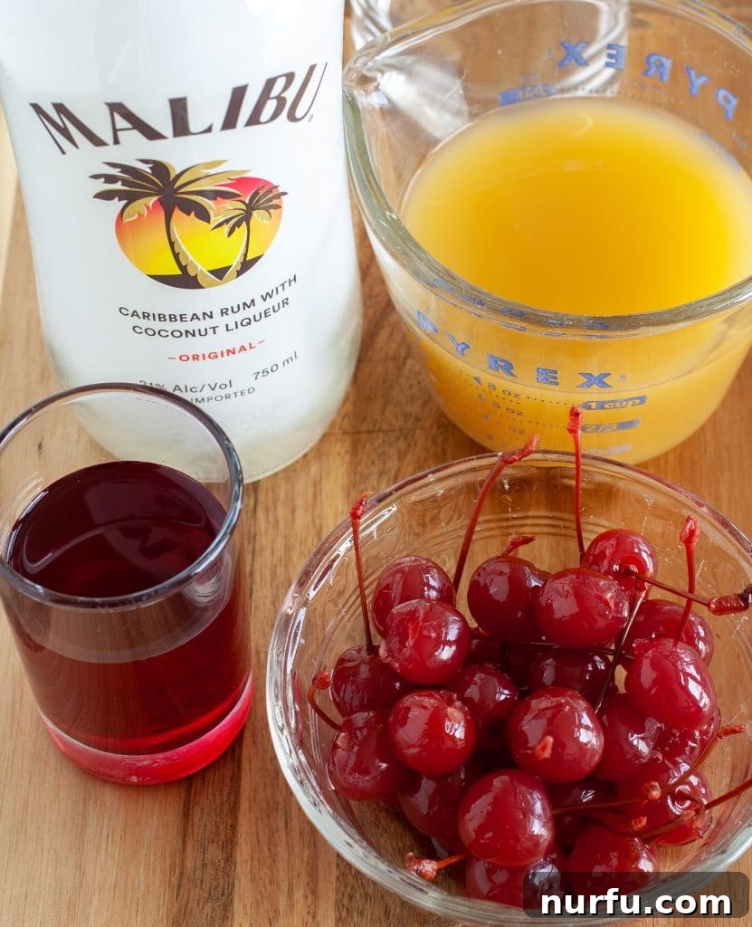 bottle of malibu rum, pineapple juice, bowl of cherries and cherry juice, neatly arranged as ingredients for a Malibu Sunset.
