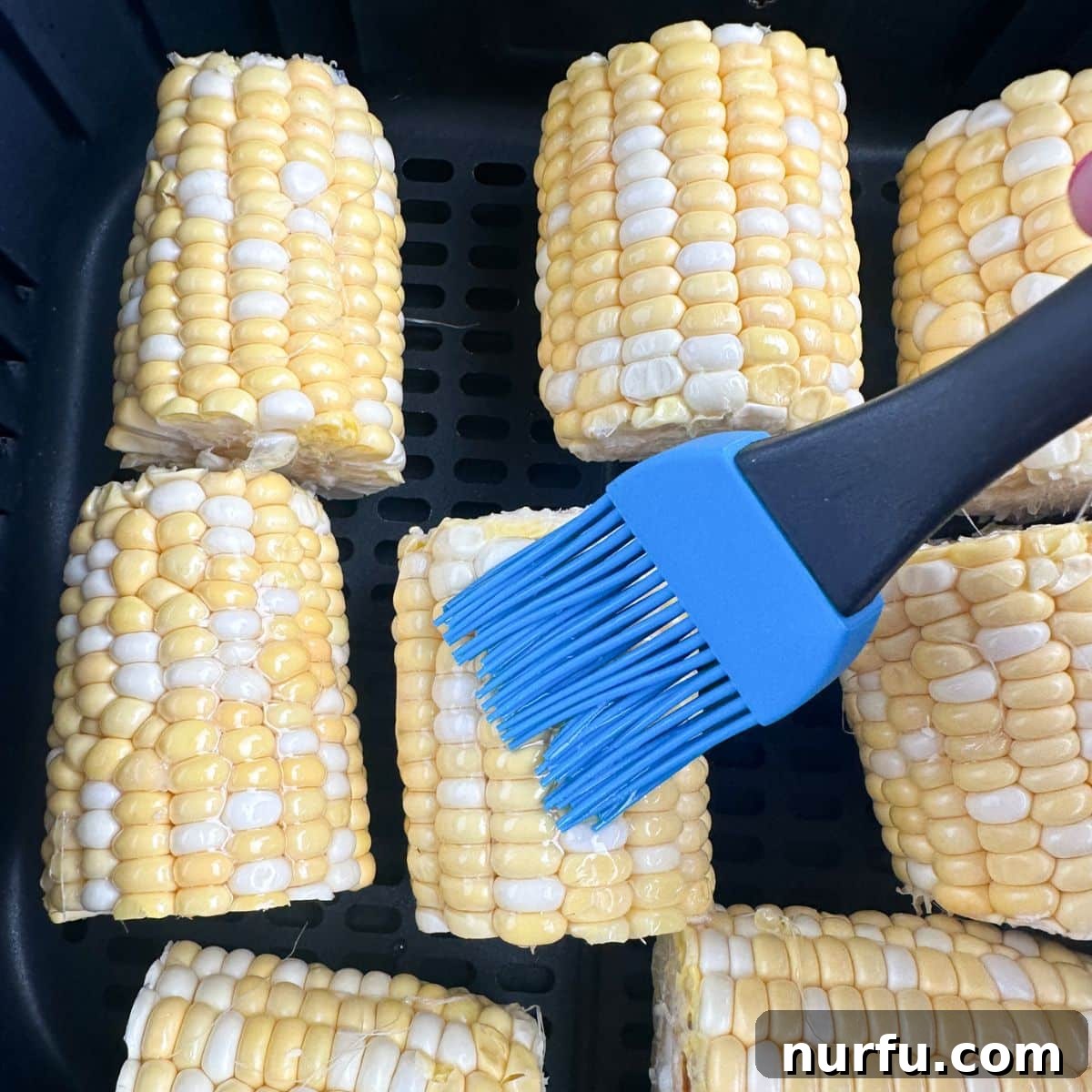Perfect Air Fryer Corn 4 Corn in air fryer basket with olive oil being brushed on.