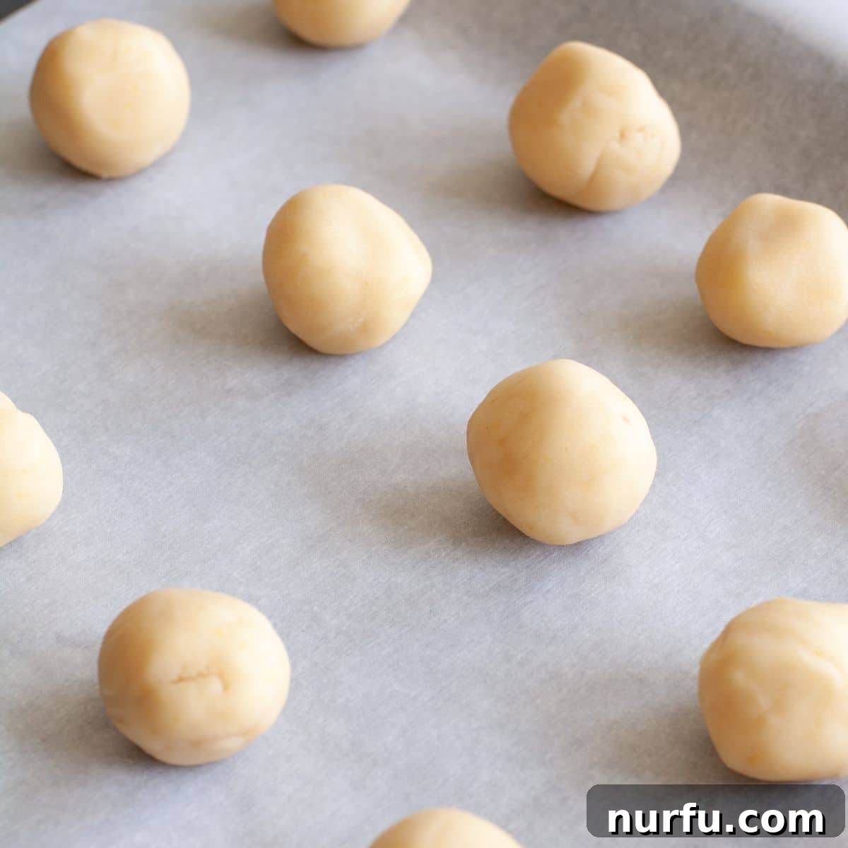 Powdered Lemon Puffs 3 Cookie dough balls on parchment paper before baking.