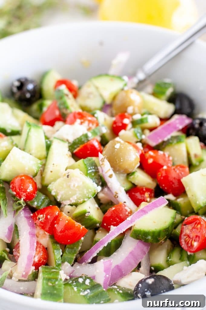 Refreshing Aegean Cucumber Medley 2 A vibrant Greek cucumber salad, featuring diced cucumbers, cherry tomatoes, red onion, crumbled feta cheese, and Kalamata olives, all tossed in a zesty lemon-oregano vinaigrette, served in a rustic ceramic bowl with a fork, ready to be enjoyed.