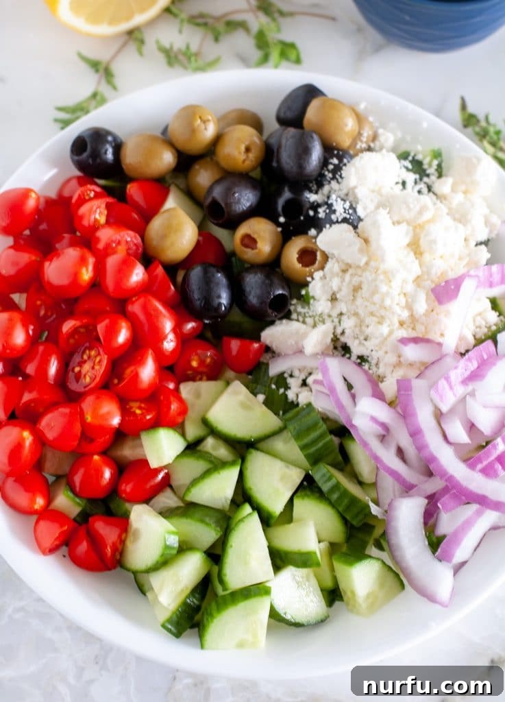 Refreshing Aegean Cucumber Medley 4 Various fresh ingredients for a Greek cucumber salad arranged in a bowl, including sliced cucumbers, halved cherry tomatoes, thinly sliced red onion, black Kalamata olives, and crumbled feta cheese, showcasing the vibrant colors and textures before being tossed.