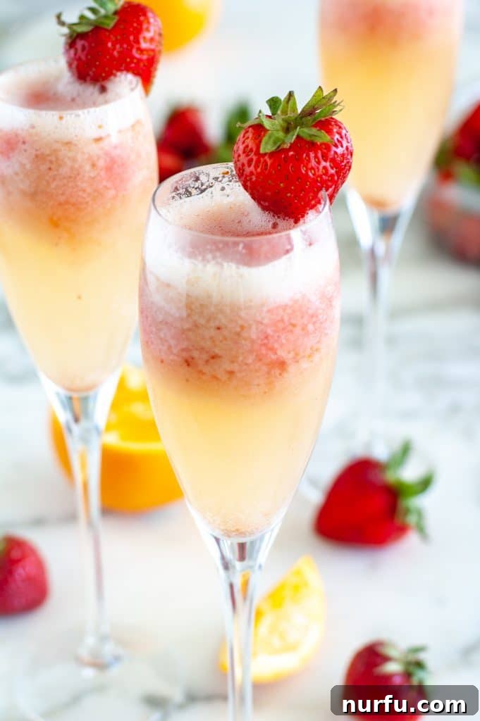 Close-up of a glass of Strawberry Mimosa with a fresh strawberry garnish on the rim.