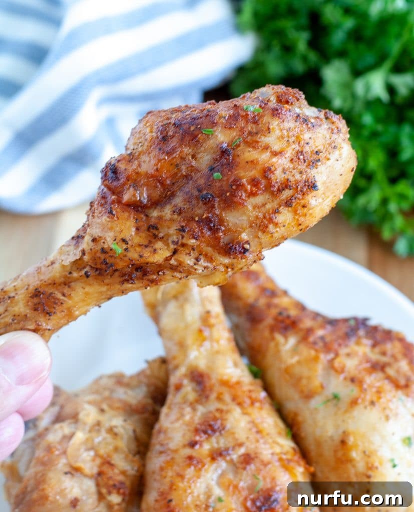 Crispy Air Fryer Drumsticks 2 Crispy chicken drumstick being held above a plate, showcasing its golden-brown skin