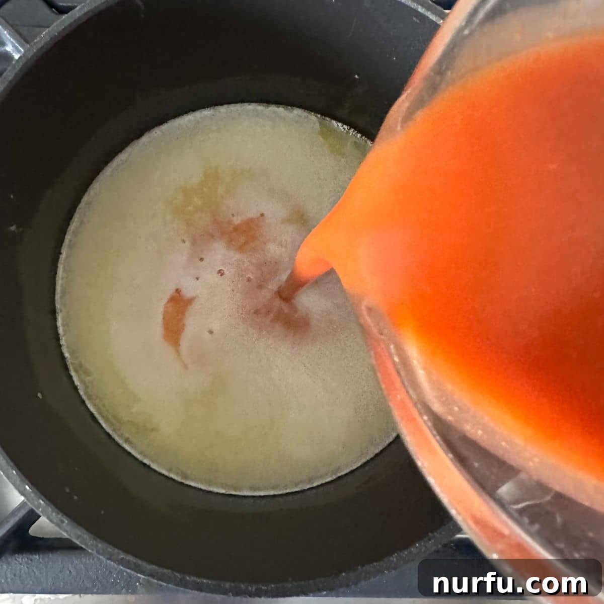 Easy Homemade Buffalo Sauce 5 A stream of red hot sauce being poured into a saucepan of melted butter, beginning the whisking process for homemade buffalo sauce.