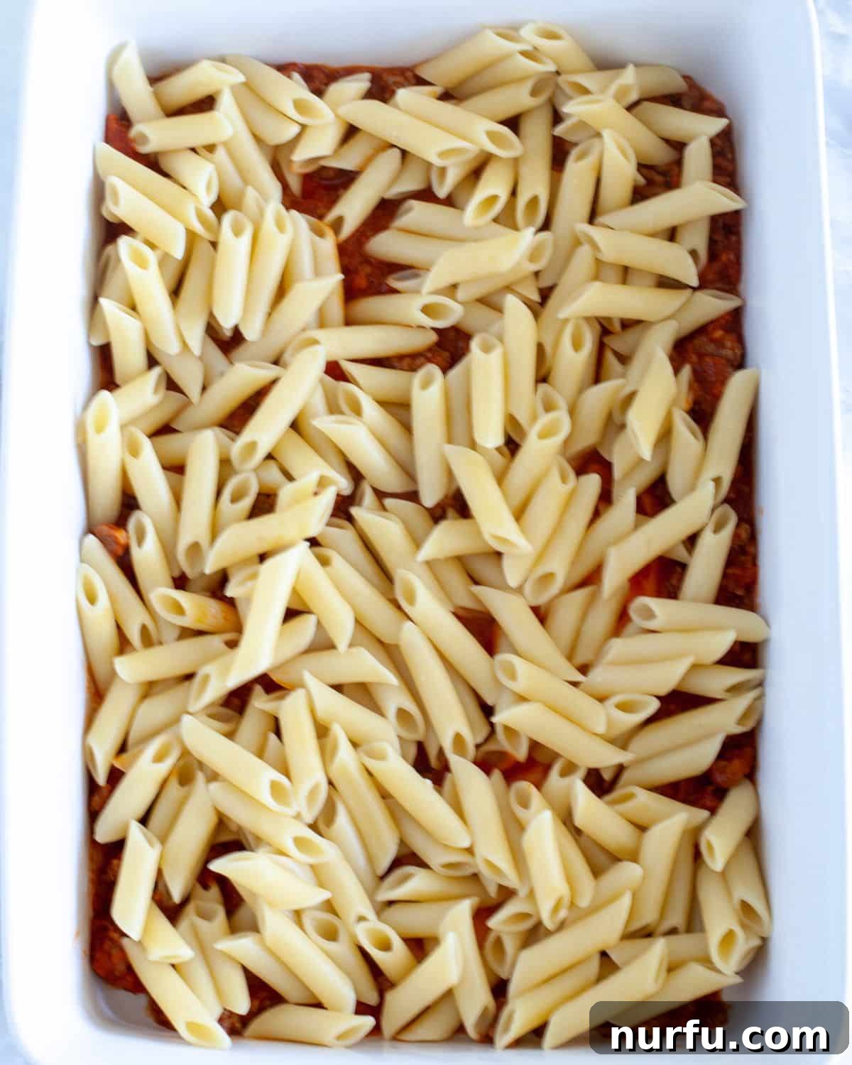 Cheesy Baked Mostaccioli 4 Layering the first half of the meat sauce in a baking dish for baked mostaccioli.