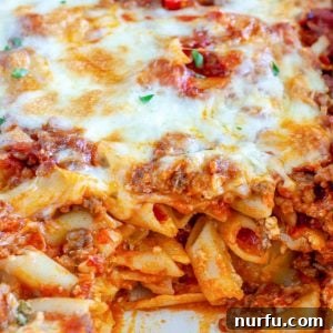 Baked Mostaccioli in a casserole dish, a vibrant red sauce with melted cheese and herbs.