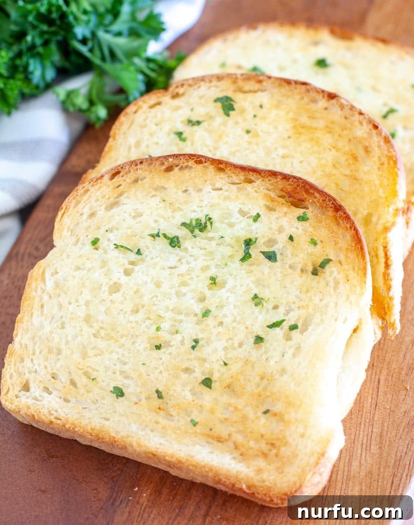 Perfect Air Fryer Texas Toast 2 Three pieces of golden-brown air fryer Texas toast with melted garlic butter, garnished with fresh parsley, resting on a rustic wooden board.
