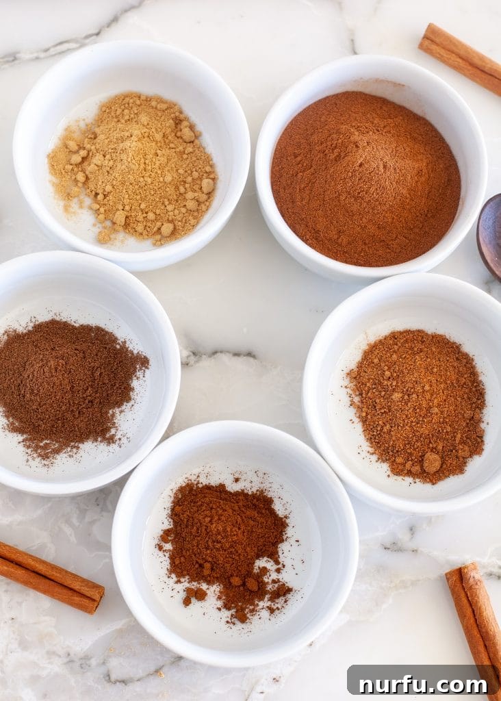 Signature Pumpkin Spice Blend 3 Various spices in separate small bowls, alongside cinnamon sticks, highlighting the individual ingredients of pumpkin pie spice.