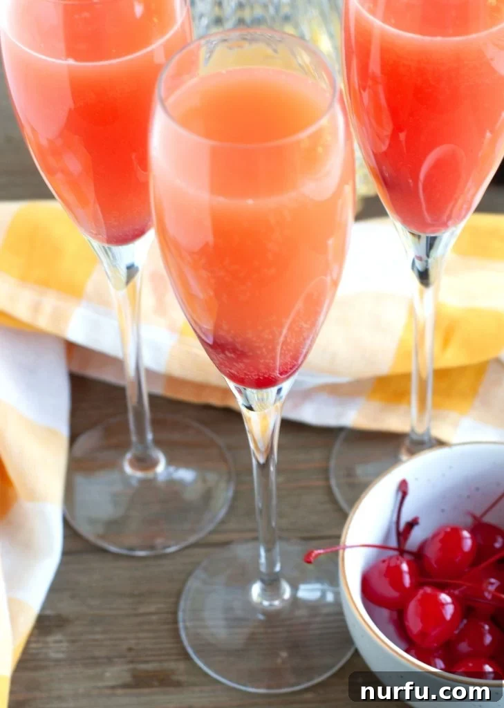 Three beautifully presented glasses of blushing mimosas, accompanied by a bowl of fresh cherries, ready for serving.