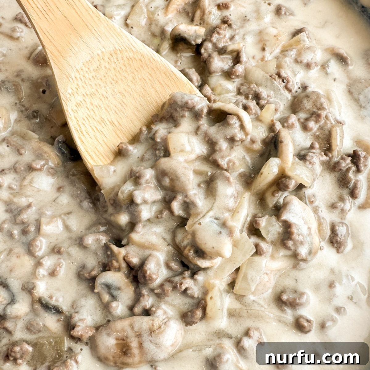 Homemade Skillet Stroganoff with Noodles 6 Wooden spoon stirring ground beef stroganoff in a skillet.