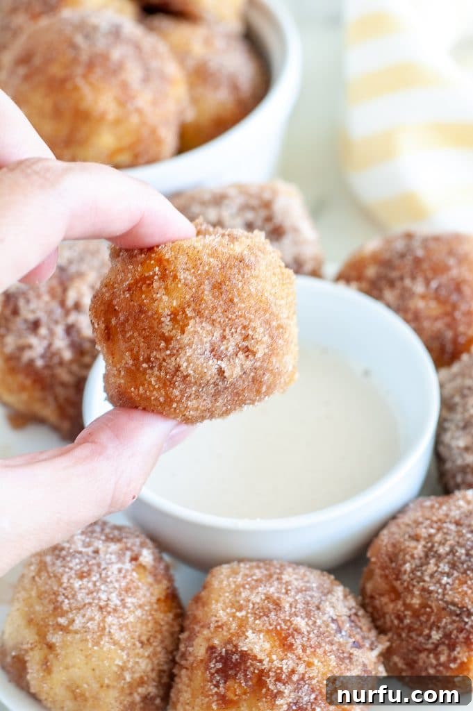 A hand holding a freshly baked, buttered, and cinnamon-sugared soft pretzel bite
