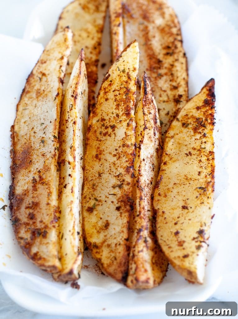 Crispy Air Fryer Potato Wedges 2 Crispy golden potato wedges on a white plate, garnished with fresh herbs, ready to be served as a tasty side dish or appetizer.