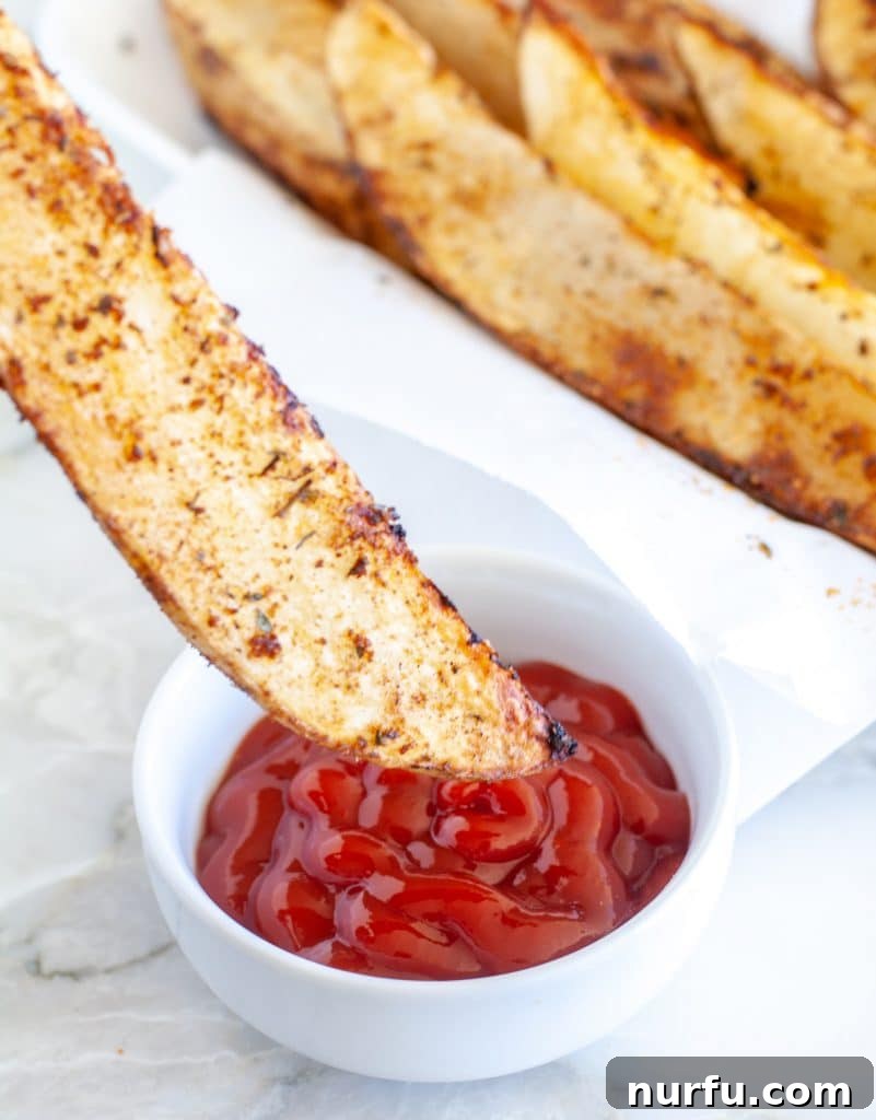 Crispy Air Fryer Potato Wedges 4 Close-up of a crispy air fryer potato wedge dipped in red ketchup, showcasing its golden color and inviting texture.