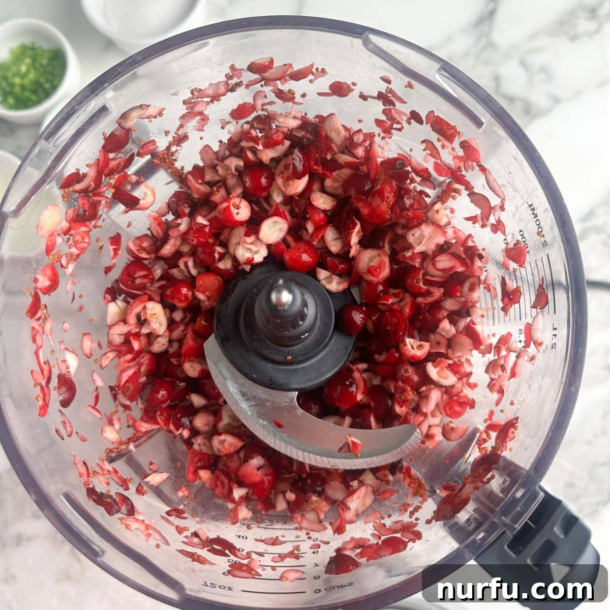 Food processor containing finely chopped cranberries, ready for the next step in making the dip.