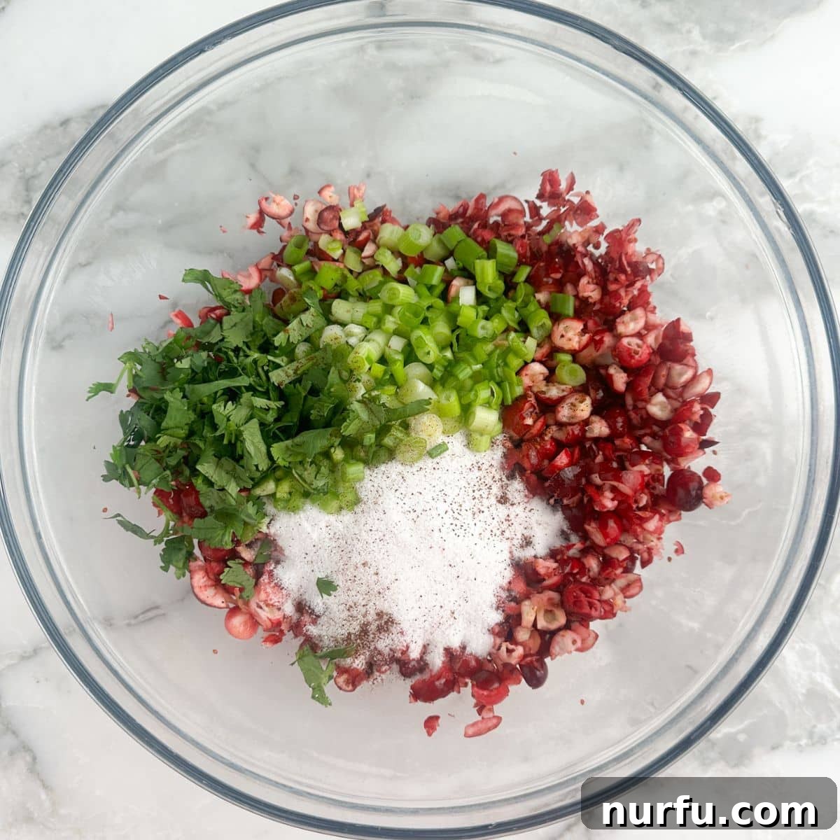 Bowl filled with mixed chopped cranberries, sugar, jalapenos, and cilantro, ready to be chilled.