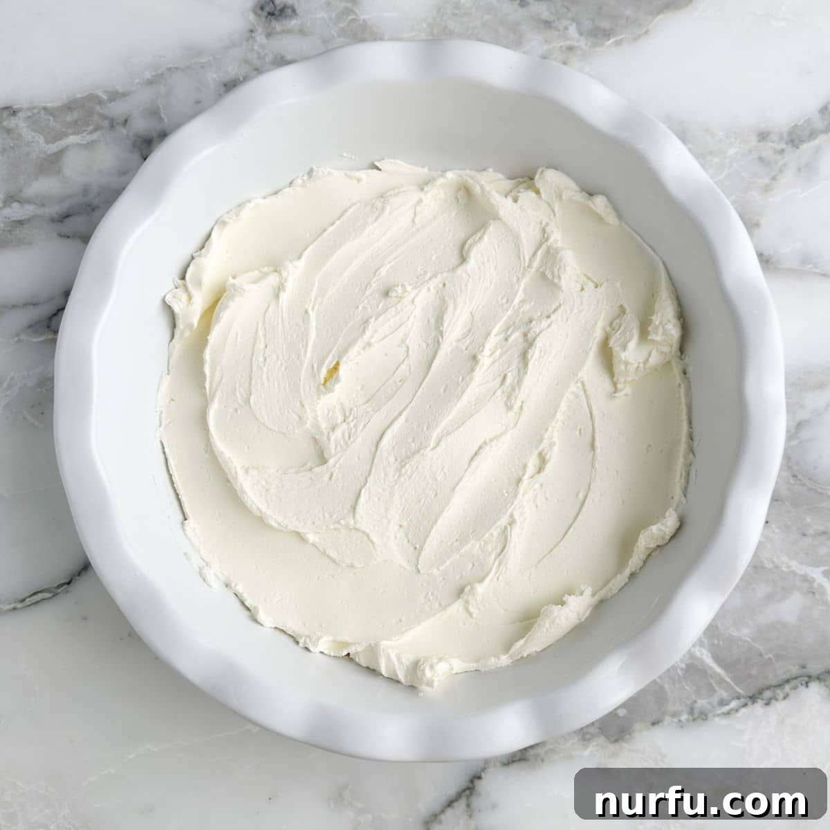 Cream cheese spread smoothly in a pie dish, forming the base of the dip.