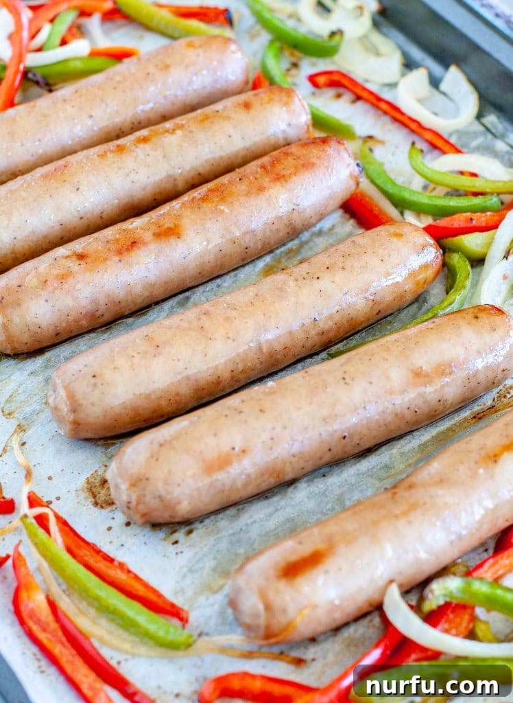 Golden Oven Brats 4 Cooked bratwurst, peppers, and onions arranged on a baking sheet, ready to be served.