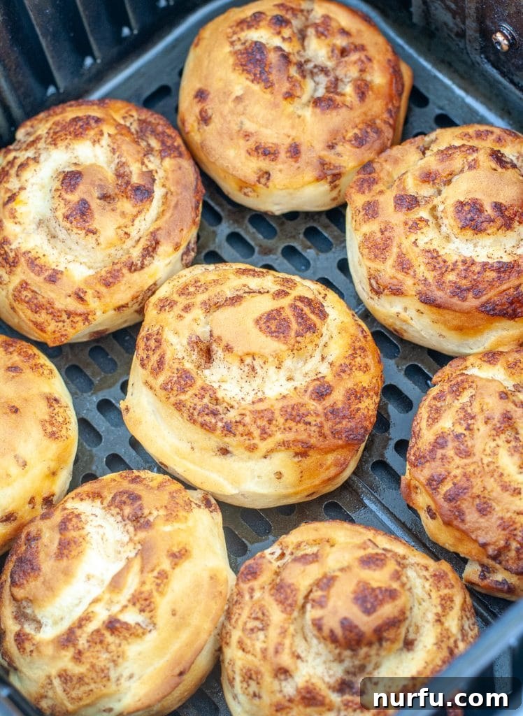 Effortless Air Fryer Cinnamon Buns 4 Cooked cinnamon rolls resting in an air fryer basket