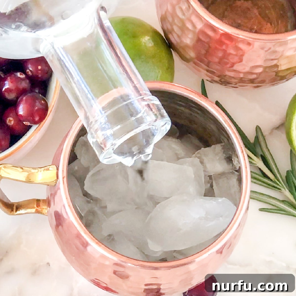 A clear glass being filled with ice, then a measure of vodka is expertly poured over it, beginning the cocktail creation process.