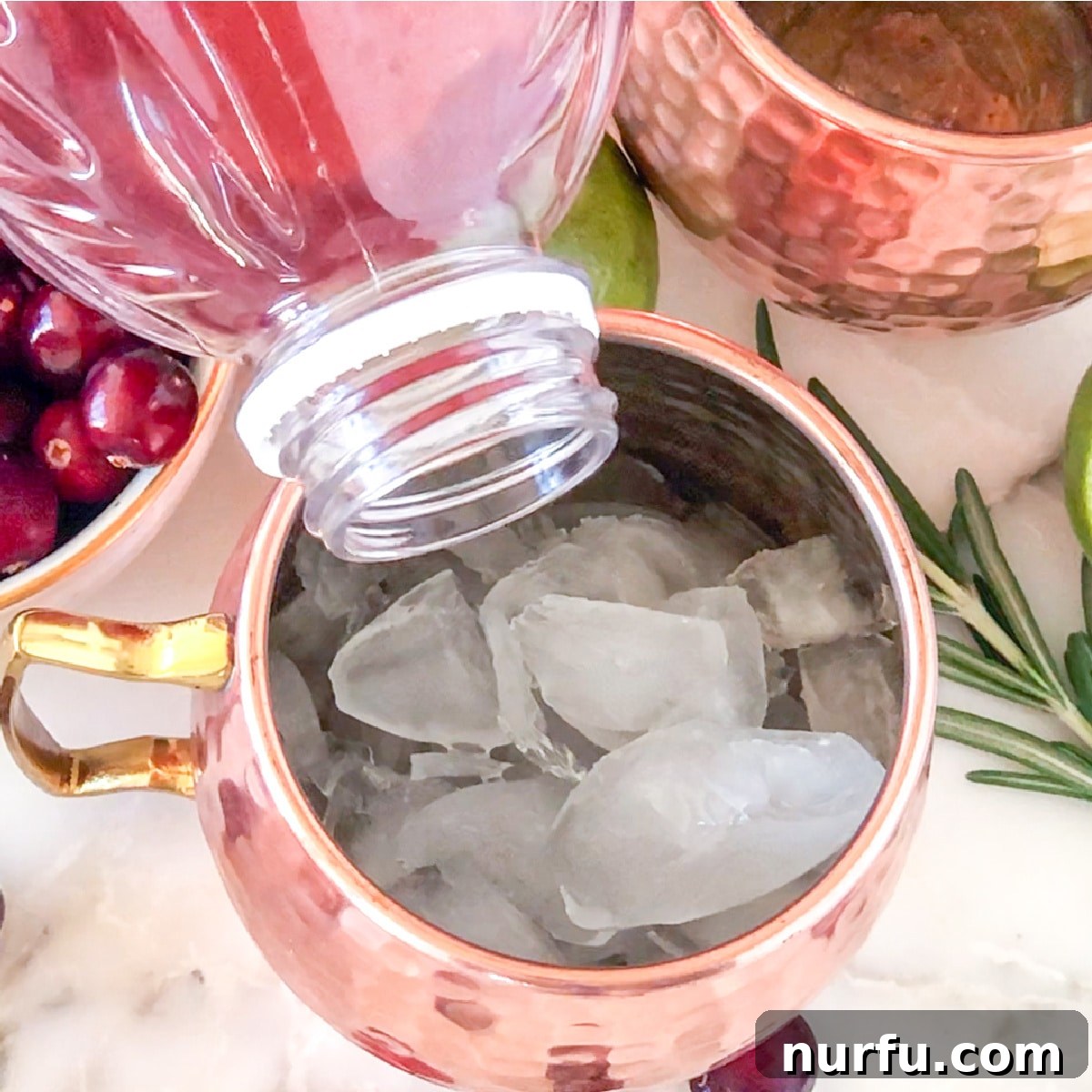 Rich red cranberry juice being poured into a glass already containing ice and vodka, adding vibrant color to the evolving Cranberry Moscow Mule.