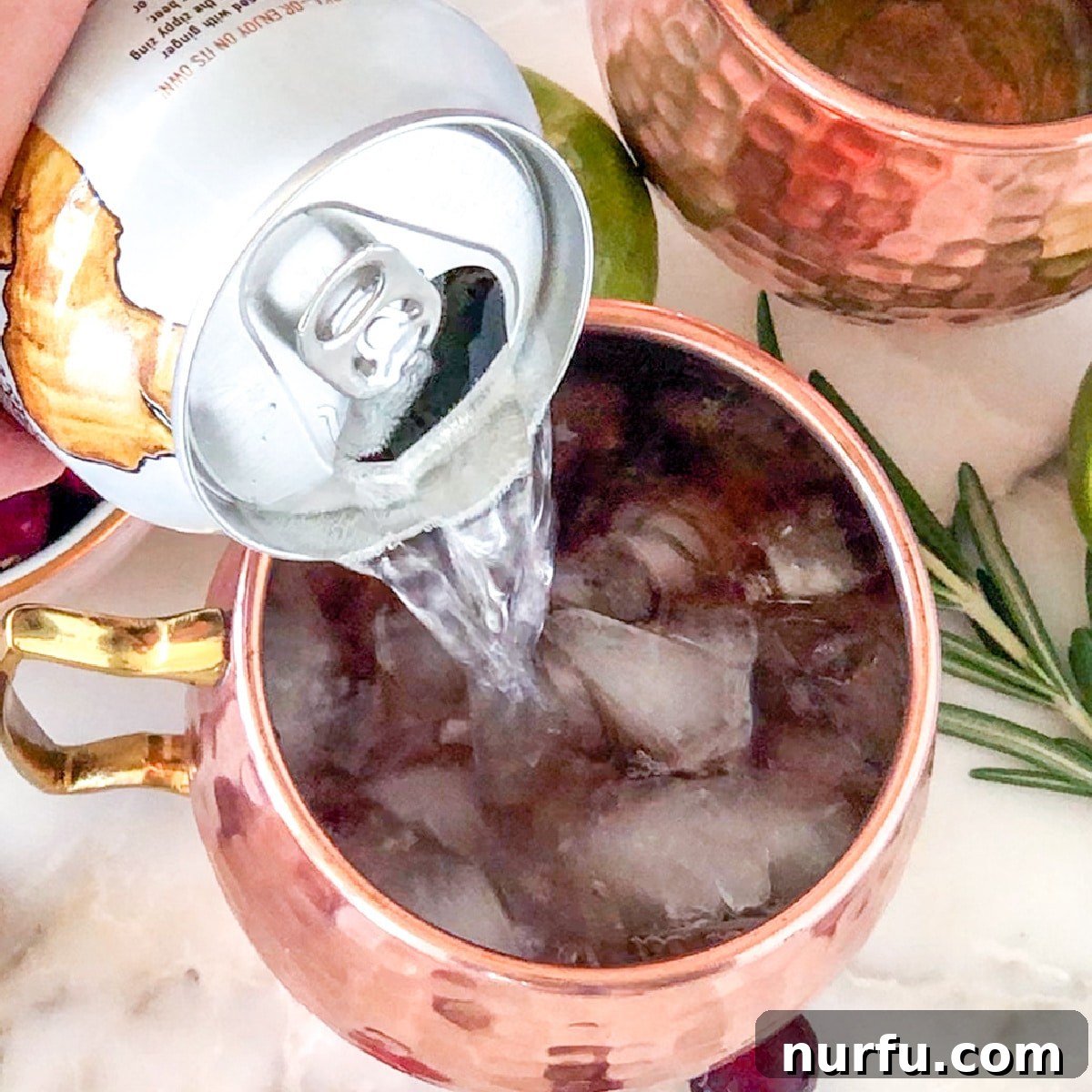 Sparkling ginger beer being poured into a cocktail glass, completing the Cranberry Moscow Mule mixture over ice.