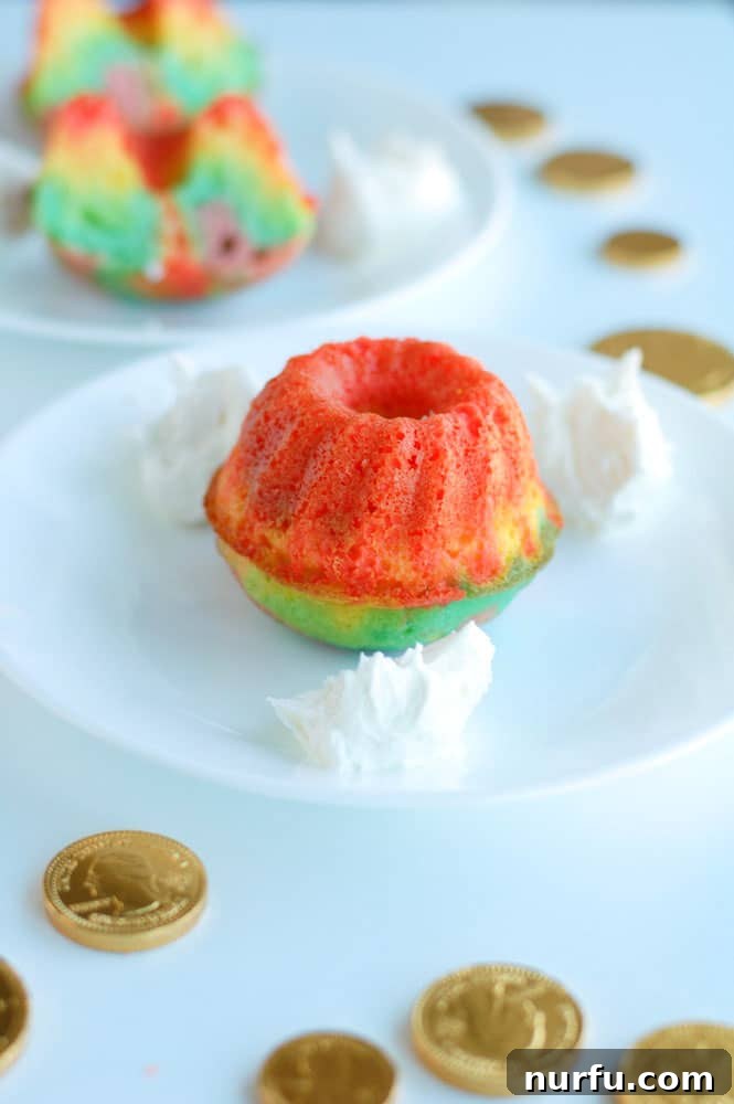 Close-up of a rainbow bundt cake showing colorful layers and a dollop of white frosting.