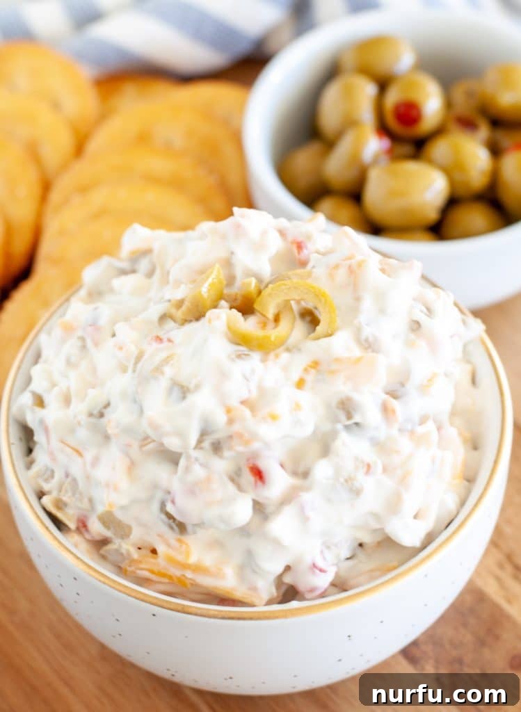 A generous bowl of creamy green olive dip, beautifully presented with a small separate bowl of whole green olives for an elegant garnish, all resting on a rustic wooden surface.