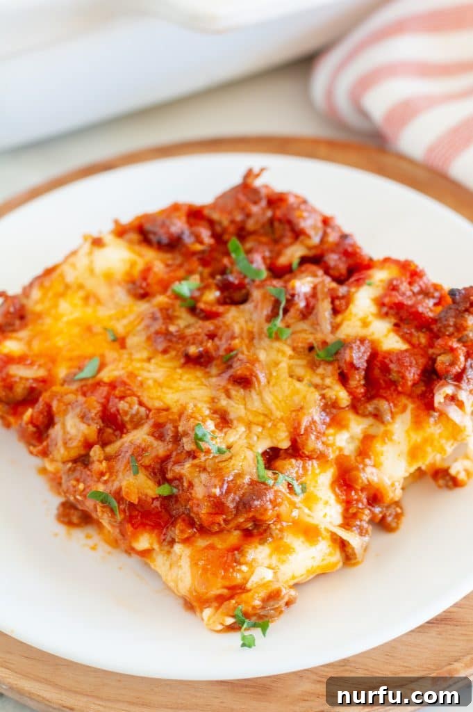 A perfectly portioned slice of no-boil lasagna, showcasing its layers of pasta, rich meat sauce, and melted cheese, served elegantly on a pristine white plate.