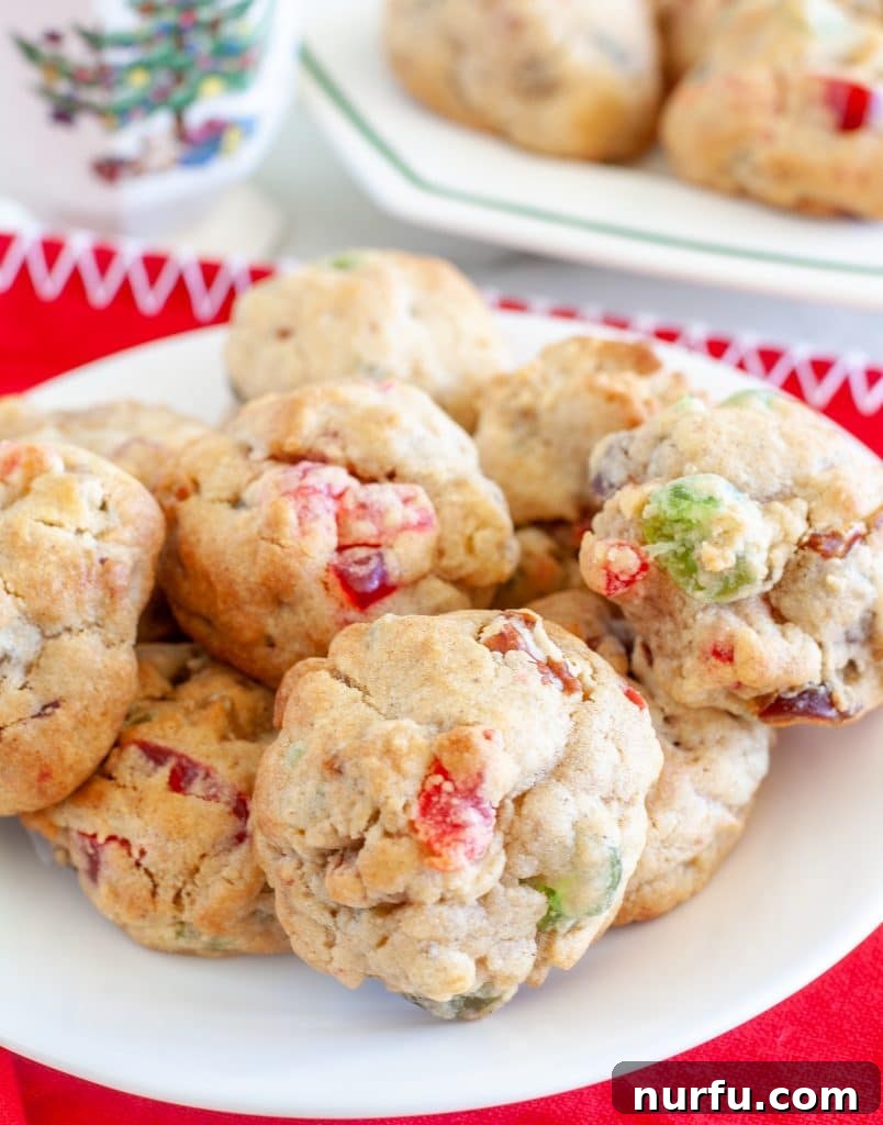 A plate piled high with festive fruitcake cookies, glistening with candied fruit and nuts, set against a warm holiday backdrop.