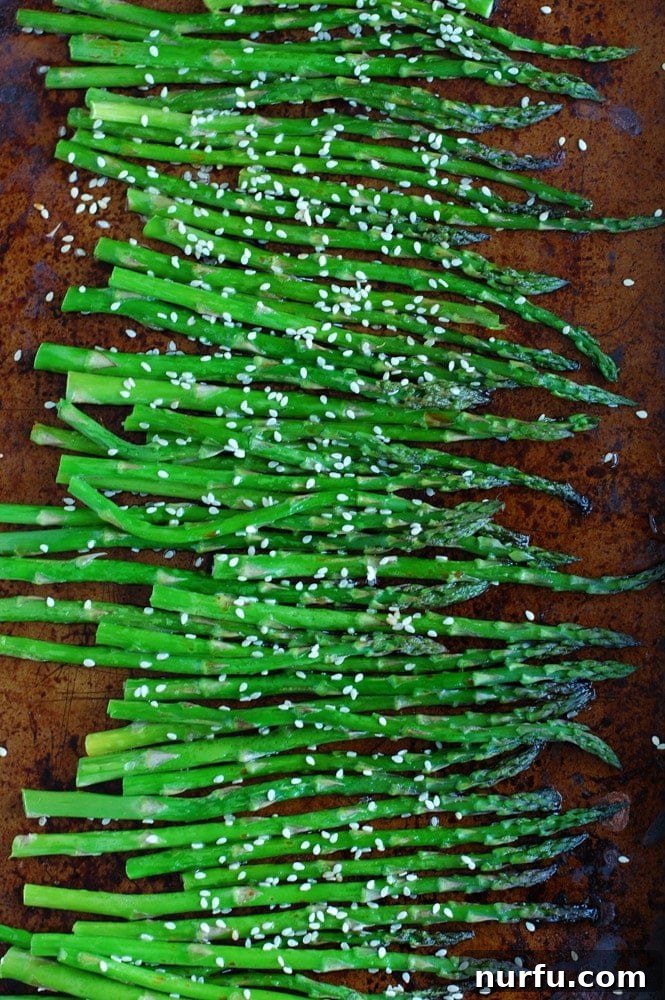 Freshly roasted asparagus with a soy sauce and honey glaze, garnished with sesame seeds, on a white serving platter.