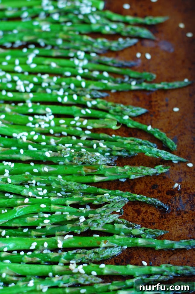 A dish of roasted asparagus with a soy and honey glaze, garnished with sesame seeds.