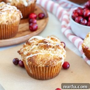 A collection of cranberry eggnog muffins, some on a plate and some in decorative paper liners, with fresh cranberries scattered around.