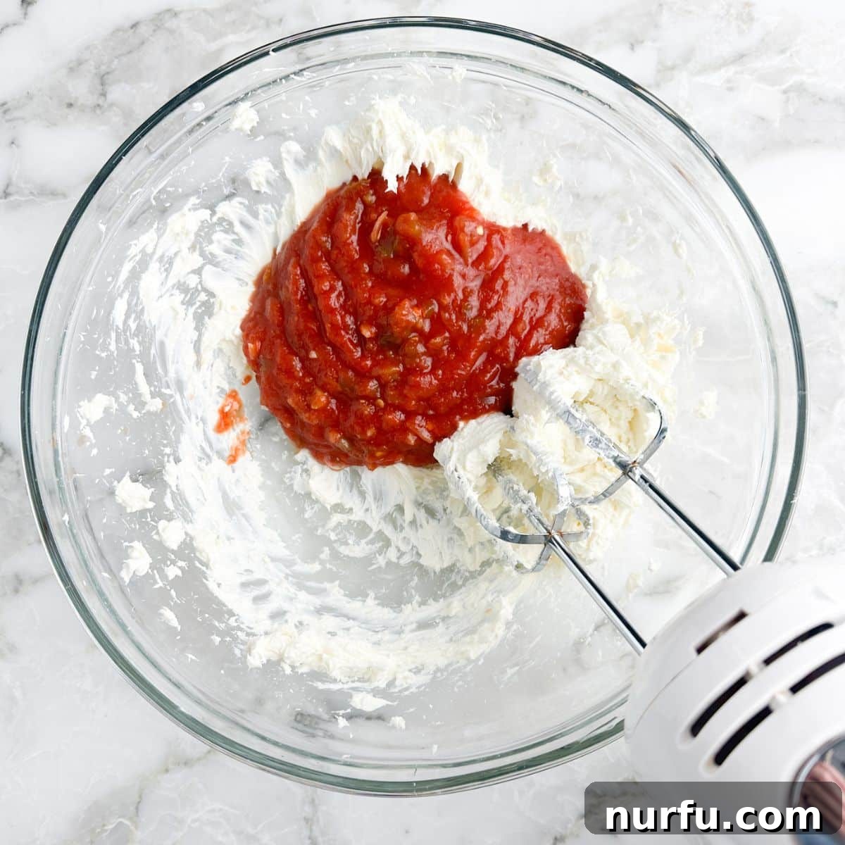 Ultimate Cream Cheese Salsa Dip 4 A bowl containing softened cream cheese and salsa, with an electric mixer poised to begin blending the two main ingredients into a delicious dip.