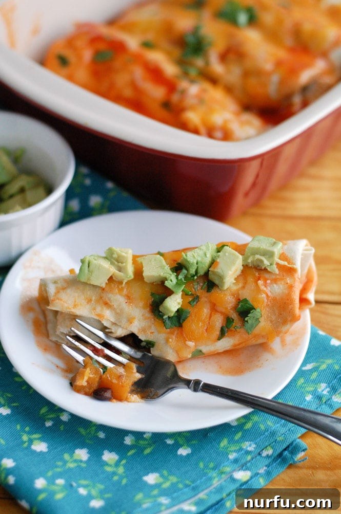 Delicious Butternut Squash and Black Bean Enchiladas A single butternut squash enchilada on a plate with a fork, and a full casserole dish in the background