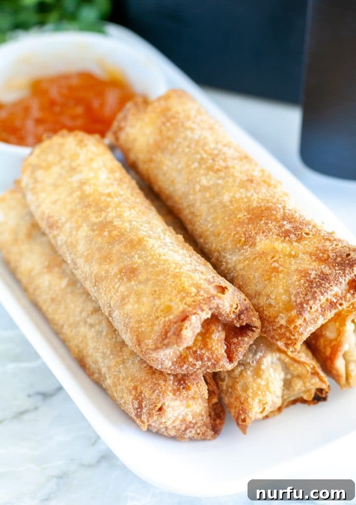 Air Fryer Crispy Egg Rolls: From Freezer to Fantastic 5 Plate with stacked egg rolls and bowl of sauce.