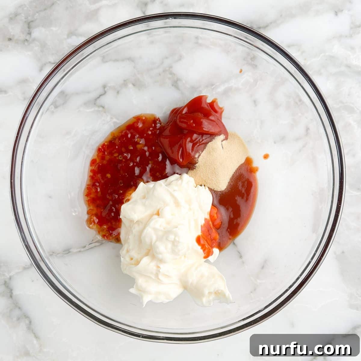 A bowl containing mayonnaise, ketchup, sweet chili sauce, and garlic powder, ready to be mixed.