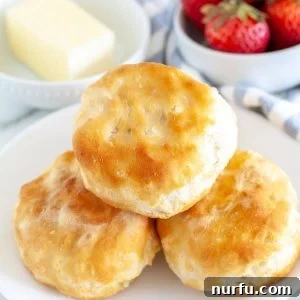 Three biscuits on a plate with bowl of butter and strawberries.