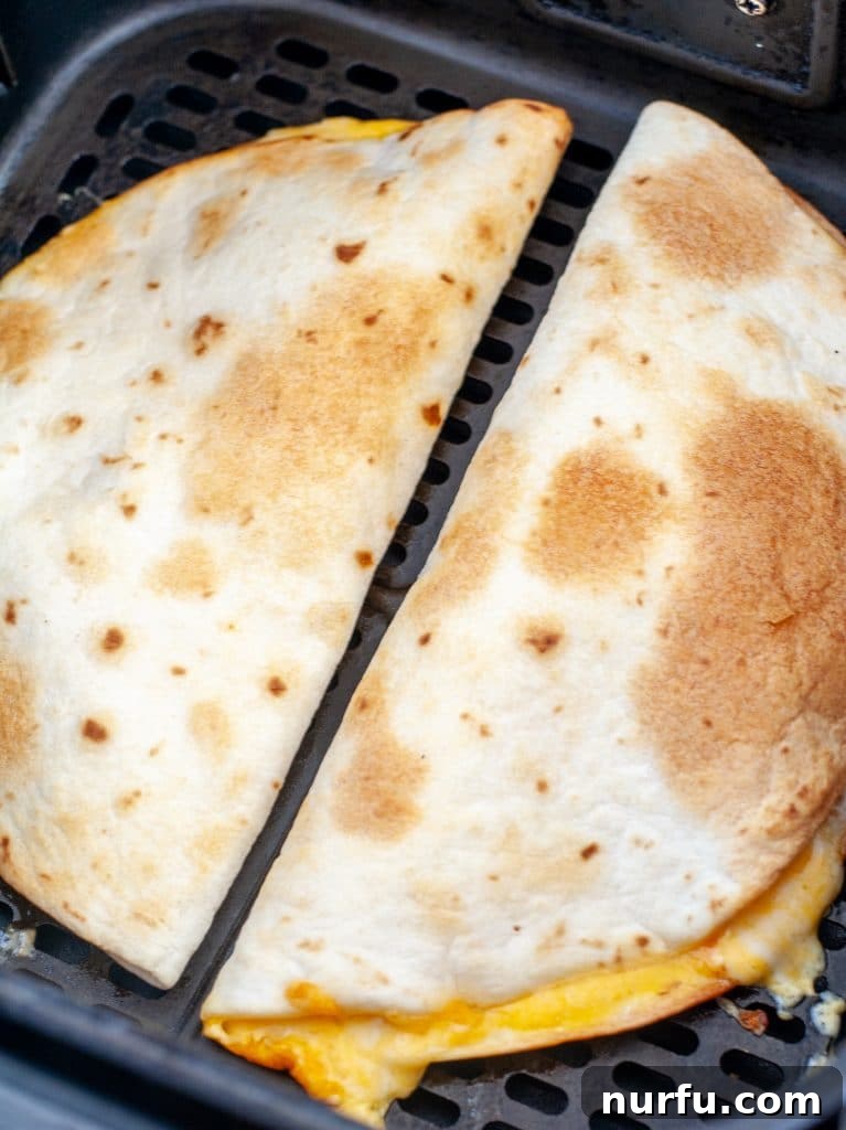 A perfectly cooked, golden-brown cheese quesadilla resting in an air fryer basket, showcasing its crispy texture.
