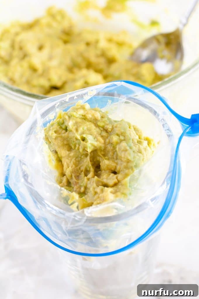 Your Guide to Freezing Guacamole 4 A freezer bag being filled with guacamole using a jar for support, demonstrating an easy filling technique.