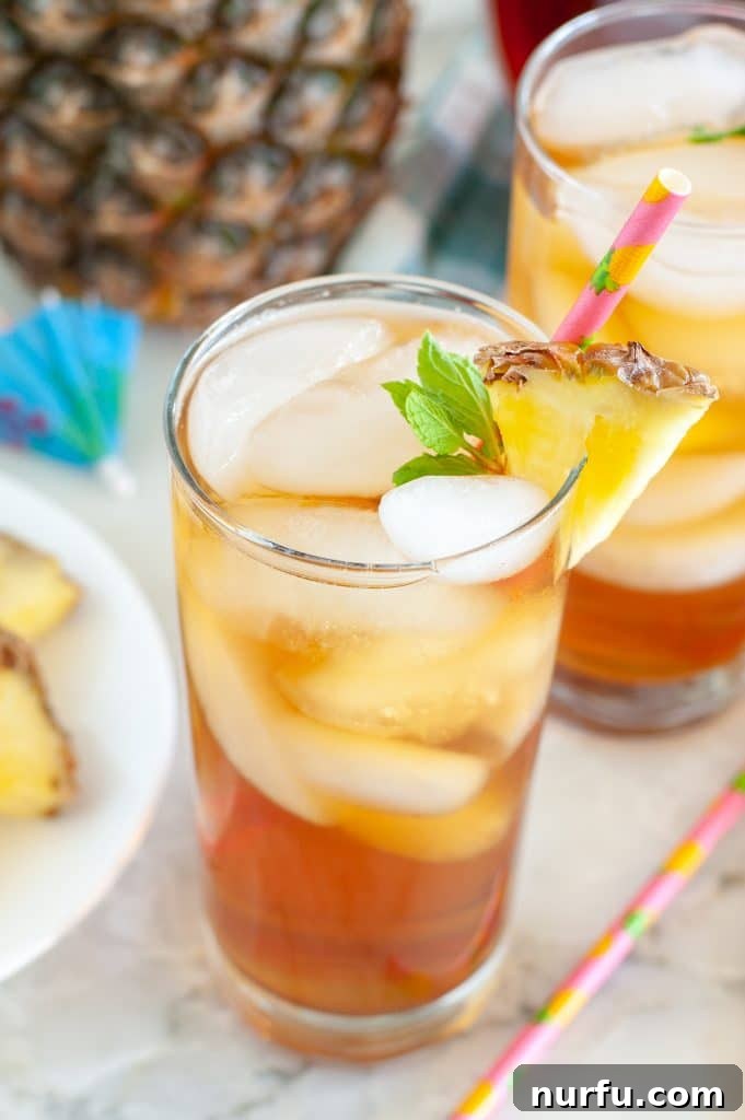 Paradise Island Iced Tea 2 Glass of Hawaiian iced tea garnished with mint and a pineapple slice, next to a plate of fresh pineapple chunks.