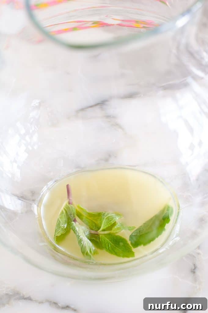 Paradise Island Iced Tea 4 A pitcher filled with a vibrant yellow liquid, showcasing fresh mint leaves, lemon slices, and pineapple chunks infusing in the sweet tea base.