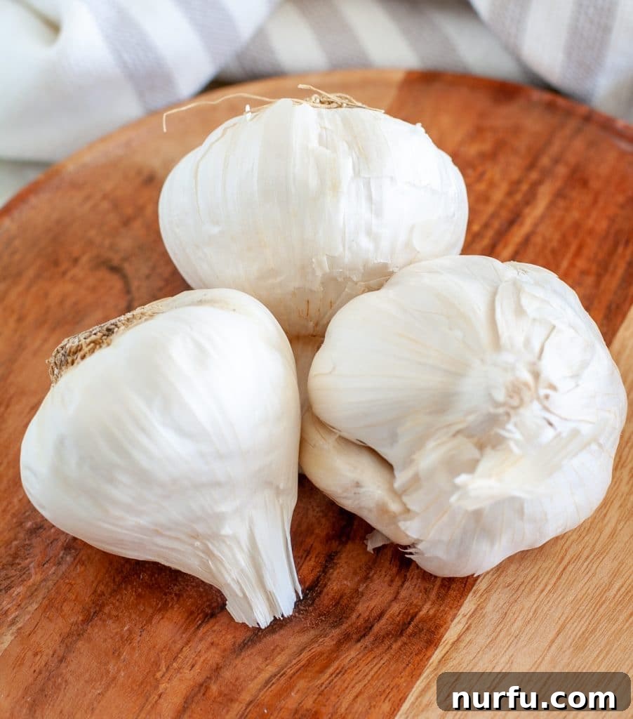 40 Glorious G-Foods 5 Three whole heads of fresh garlic, with their papery skins intact, resting on a rustic wooden plate, ready for culinary use.