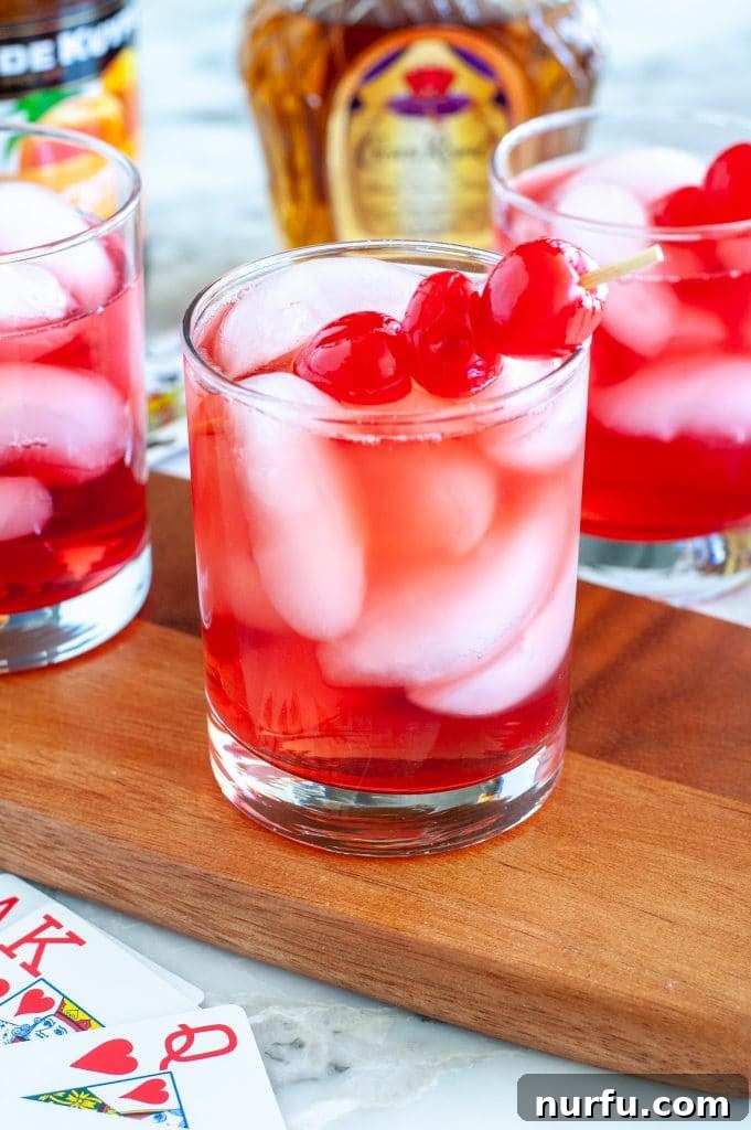 A vibrant red Royal Flush cocktail served in a highball glass, garnished with two glistening maraschino cherries, set against a stylish, slightly blurred background.