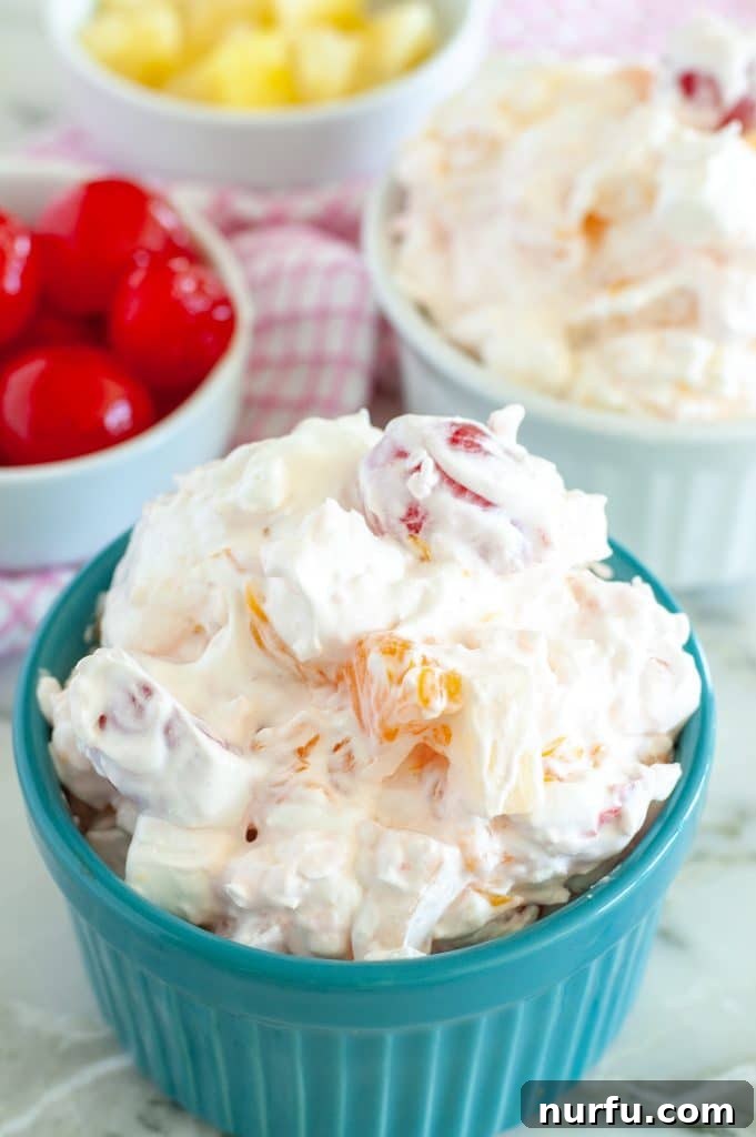 Heavenly Ambrosia Fluff 2 A beautifully presented fruit salad in a clear glass bowl, showcasing vibrant maraschino cherries, pineapple, mandarin oranges, and fluffy marshmallows, all coated in a creamy white dressing.