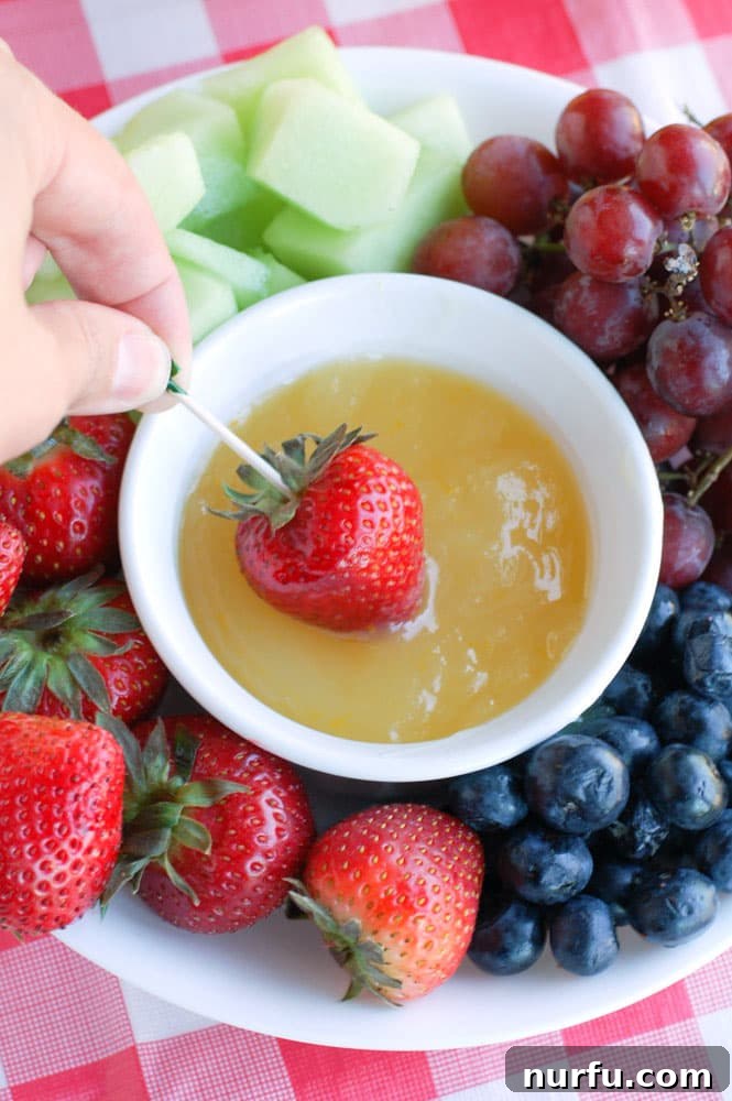 Sunny Orange Dip 4 A refreshing orange fruit dip in a glass bowl, garnished with a slice of orange and surrounded by an assortment of summer berries and melon slices.