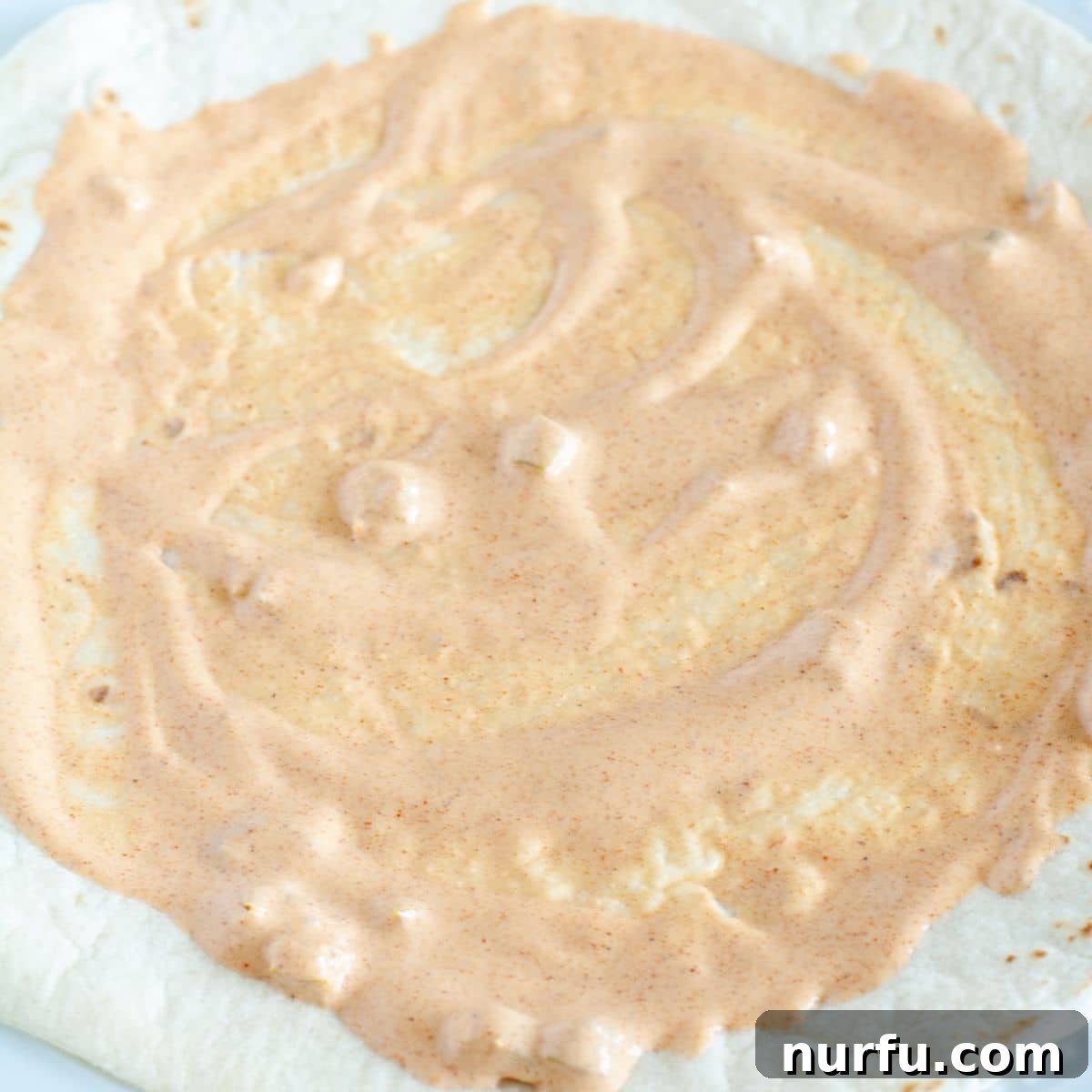 Homemade Taco Bell Chicken Quesadilla Perfection 4 A soft flour tortilla is carefully laid out with a thin, even layer of creamy quesadilla sauce spread across its surface, ready for the next delicious toppings.