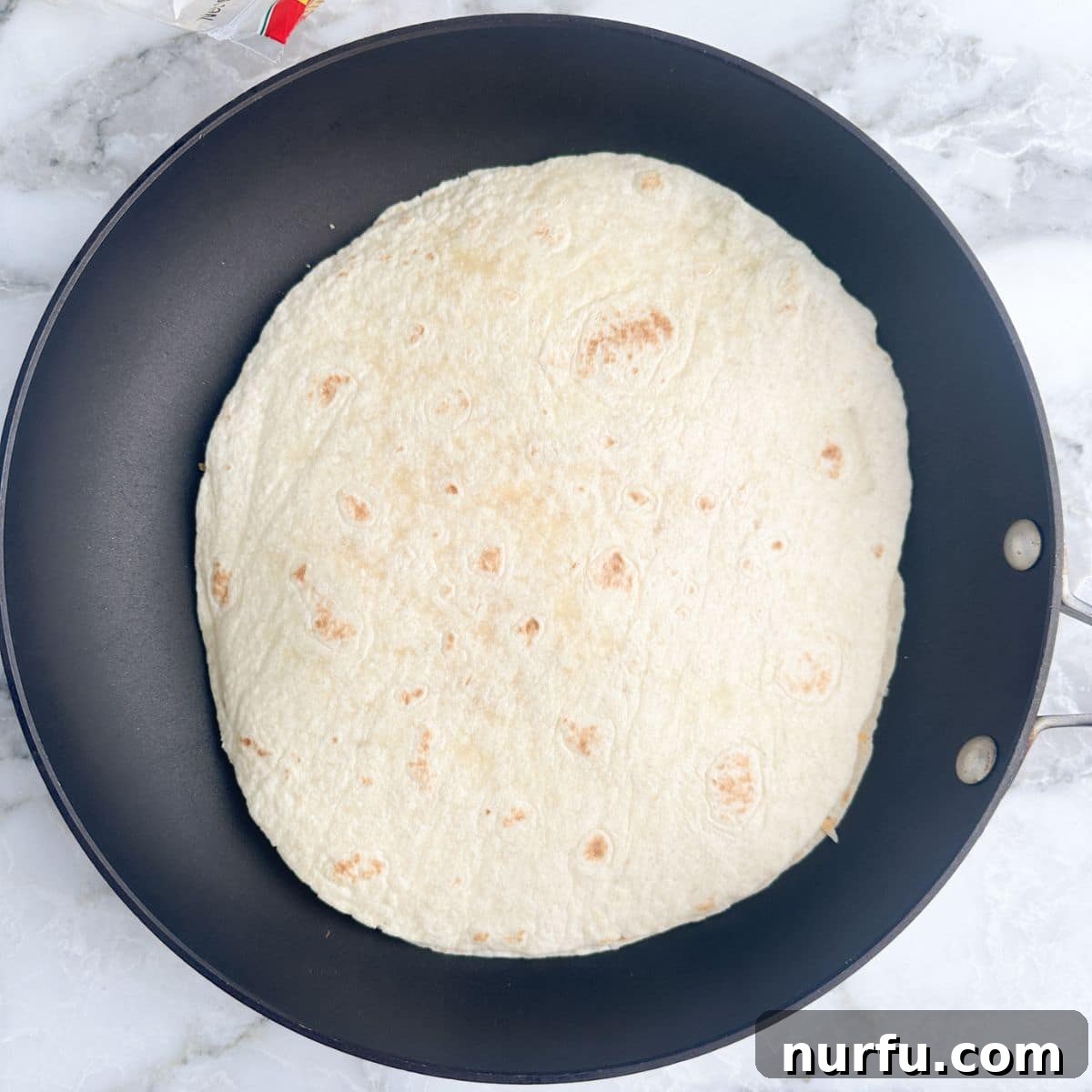 Homemade Taco Bell Chicken Quesadilla Perfection 6 An uncooked chicken quesadilla, perfectly assembled with its top tortilla, gently frying in a pan, promising a soon-to-be golden-brown finish.