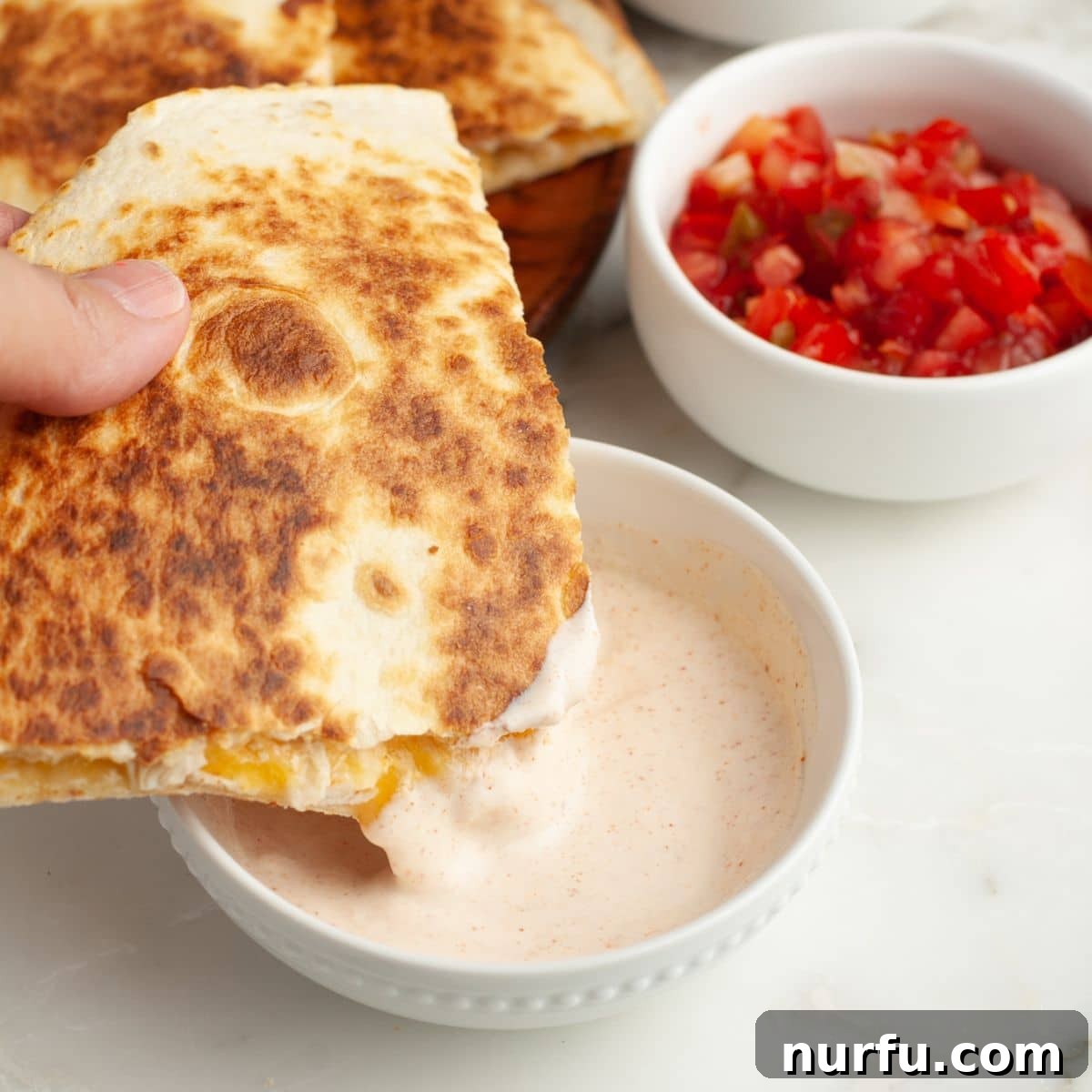 Homemade Taco Bell Chicken Quesadilla Perfection 7 A perfectly cooked chicken quesadilla, sliced into wedges, being dipped into a small bowl of creamy quesadilla sauce, highlighting its deliciousness.